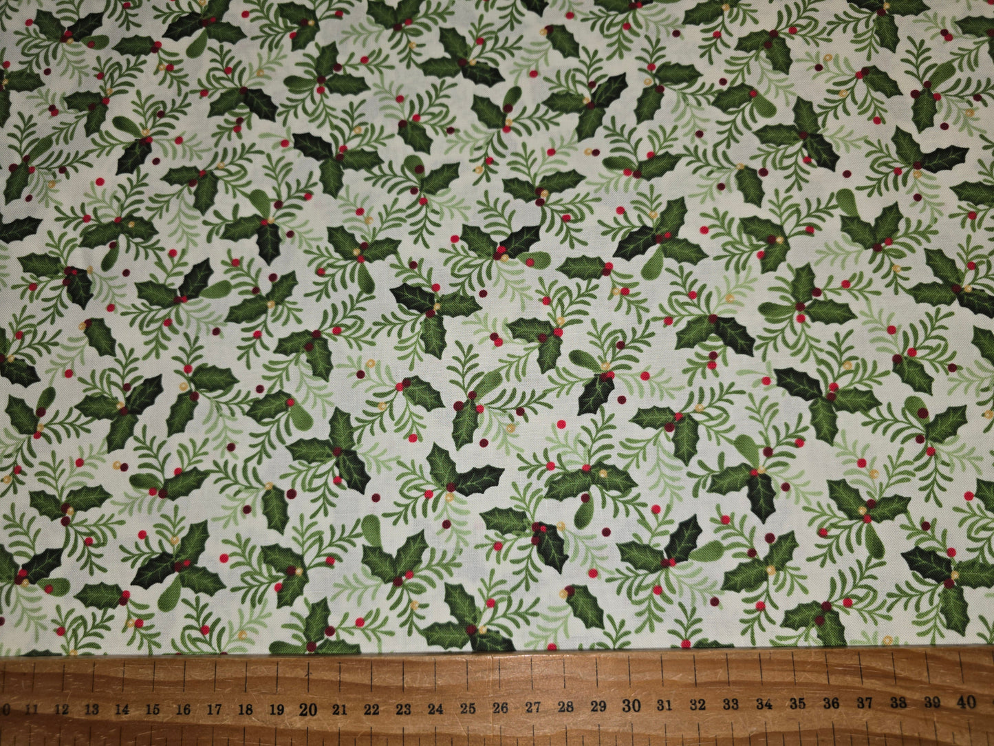 Fabric with holly leaf pattern on a white background, ruler at the bottom for scale.
